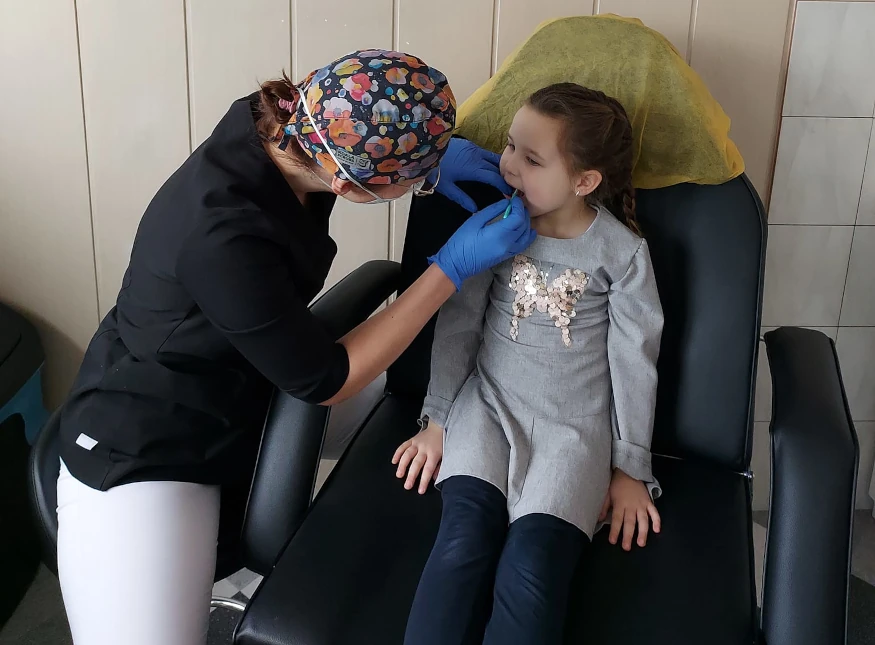 Dziewczynka z żłobka Szczecinek siedzi spokojnie podczas kontroli zębów prowadzonej przez specjalistkę.